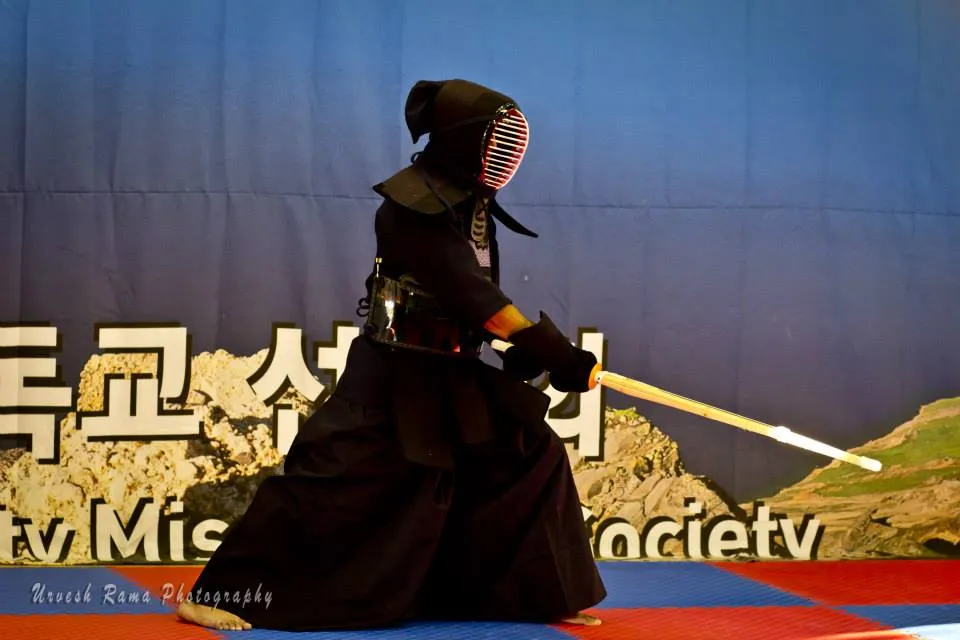 Students in dark traditional uniform holding bamboo swords in formation.