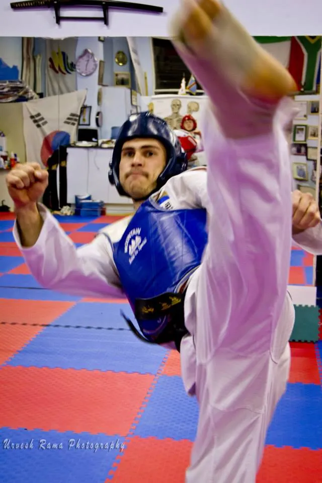 A student in sparring gear throwing a high front kick.