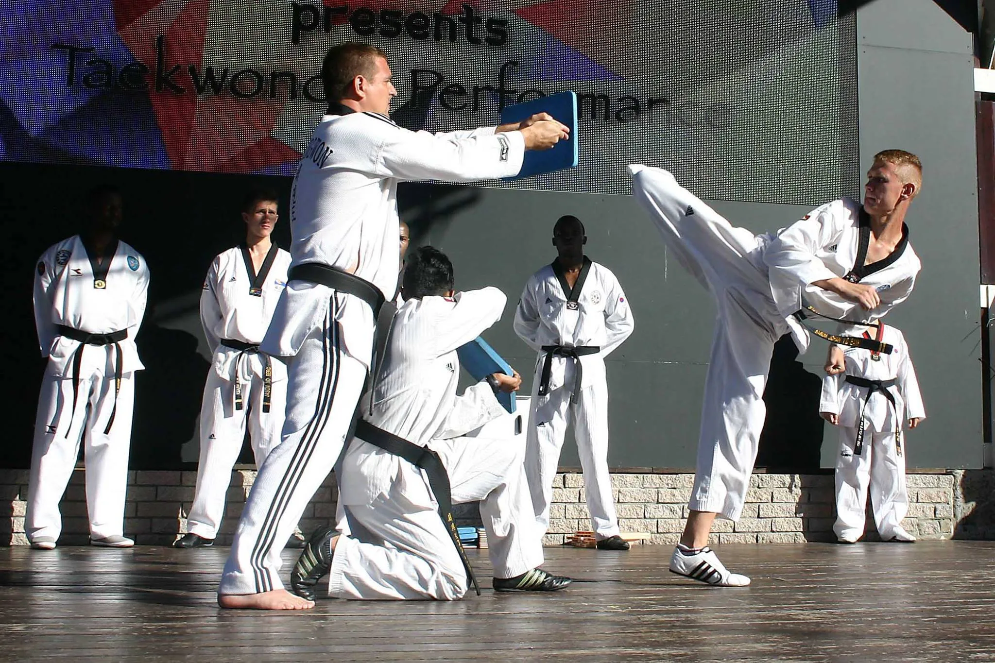 A KJD student breaking a board with a high kick at a Taekwondo performance.