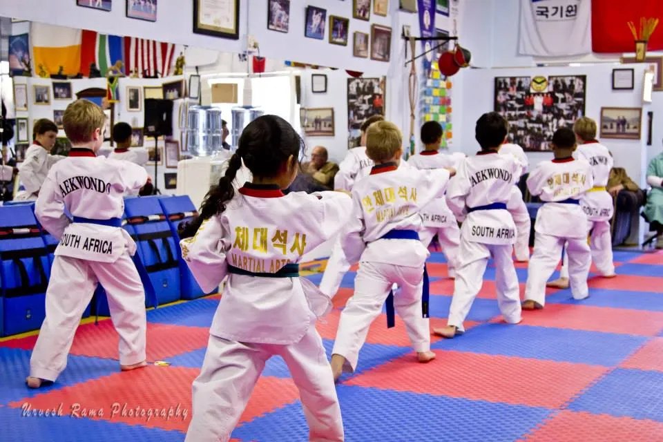 A row of children in white uniforms performing a pattern together on the dojang mats.