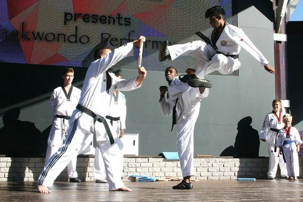A KJD student performing a flying kick towards a board at a demonstration.
