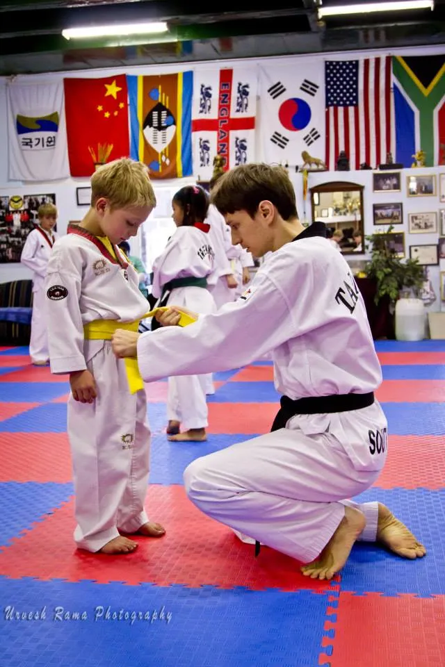 An instructor kneeling to tie a young student’s belt.