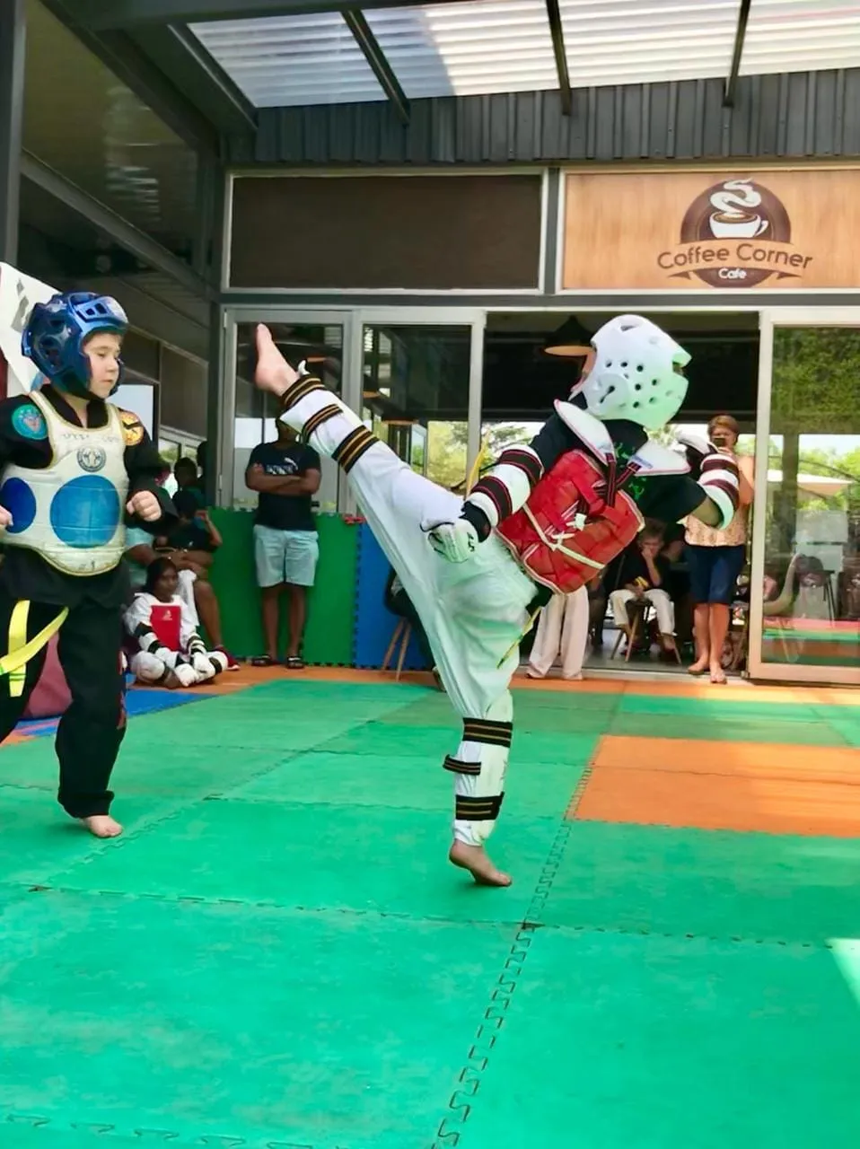 A very young student in a helmet performing a front kick onto a pad.
